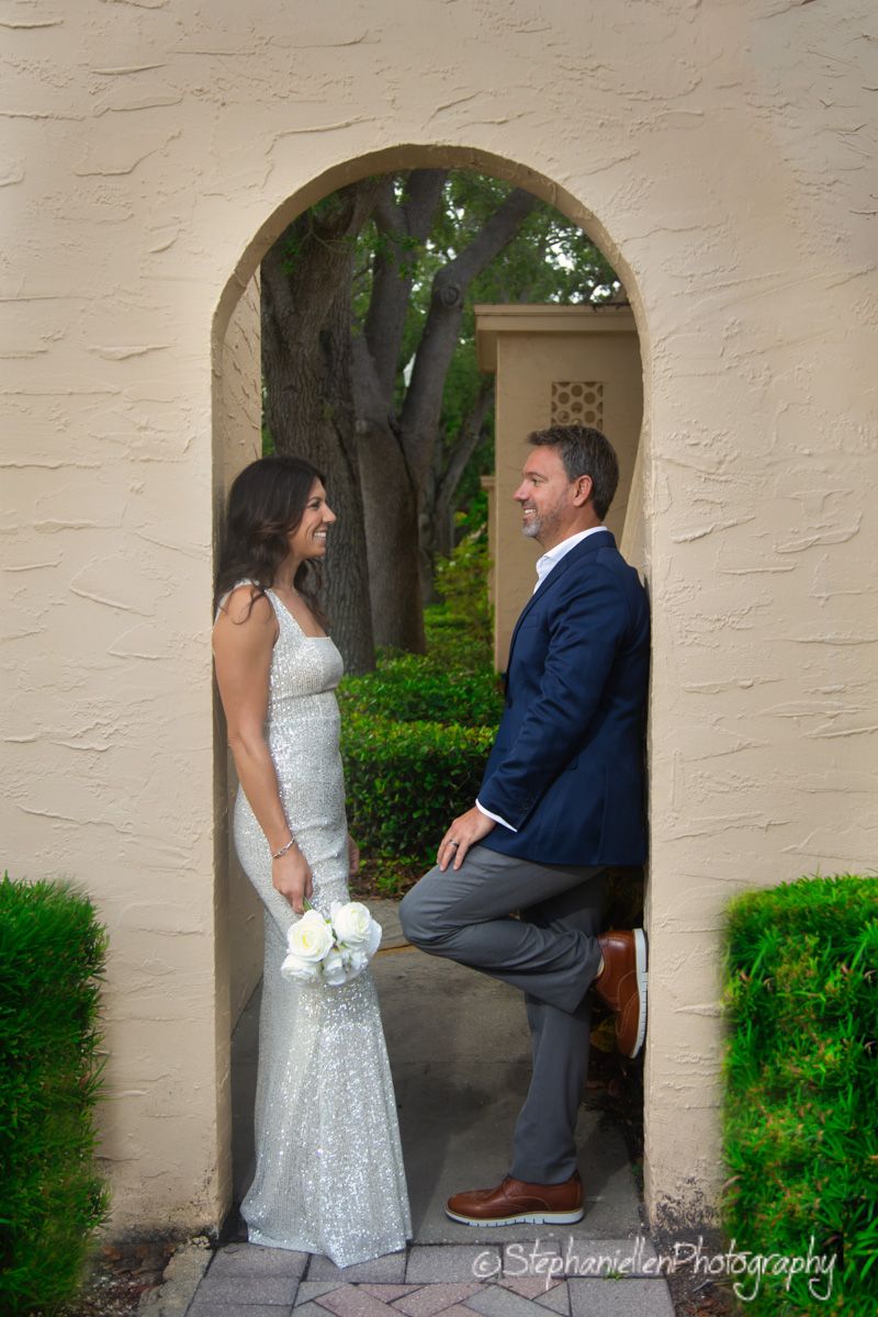 Bride and groom laughing together framed by a charming arched doorway at their outdoor wedding venue.