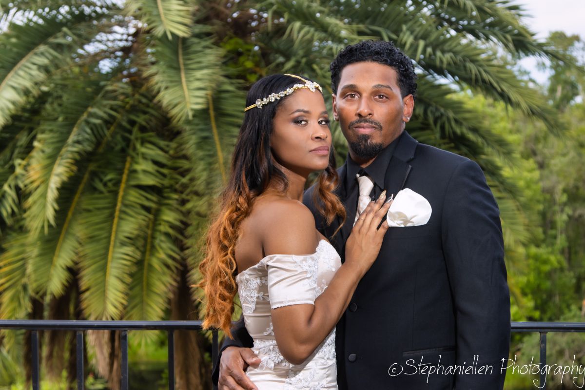 Elegant bride and groom posing together in front of tropical palm trees outdoors.