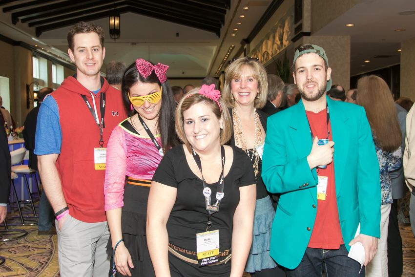 Group of five people in colorful costumes pose together at indoor themed party event.