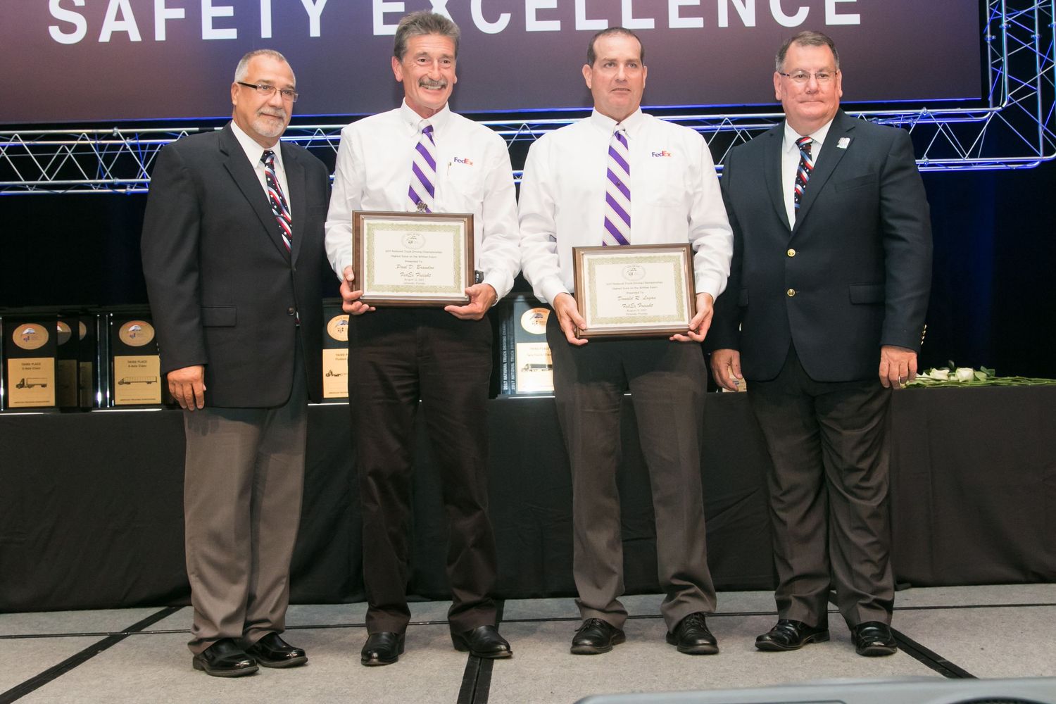 Four men pose with framed Safety Excellence award certificates at formal recognition ceremony.