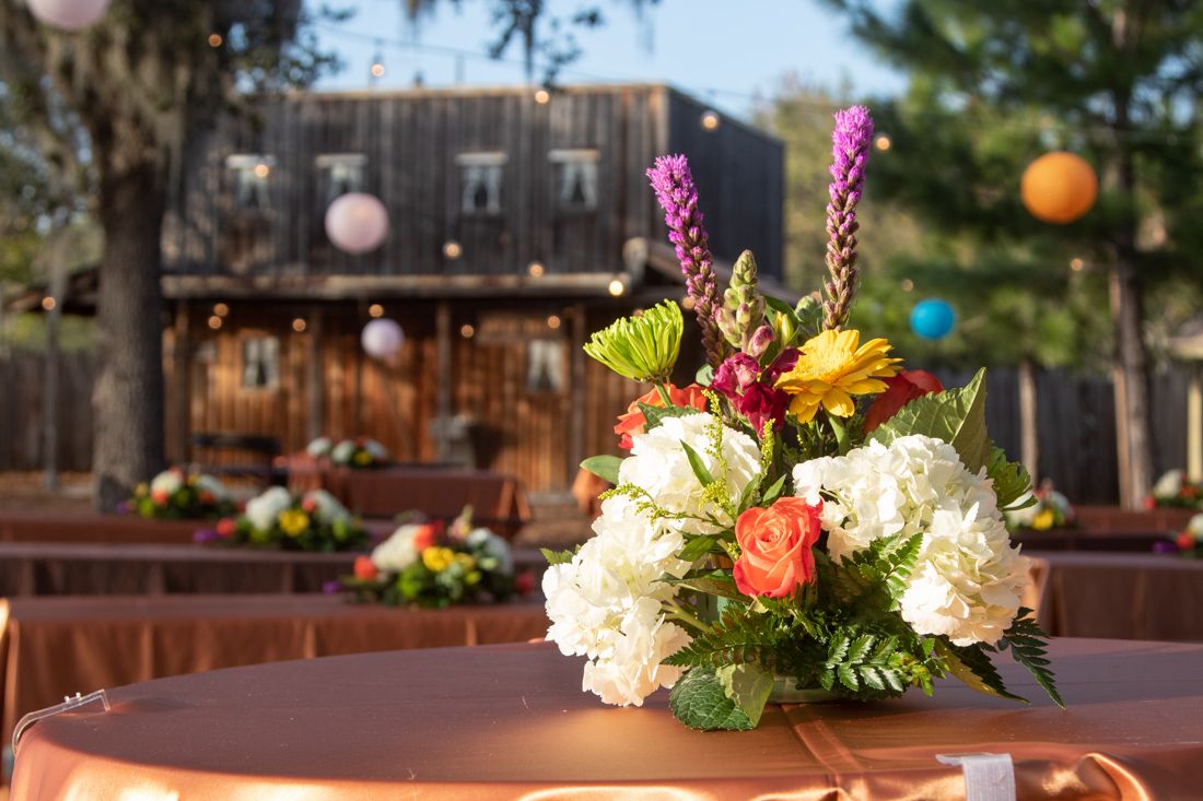 Colorful floral centerpiece on a copper tablecloth at an outdoor rustic venue event.