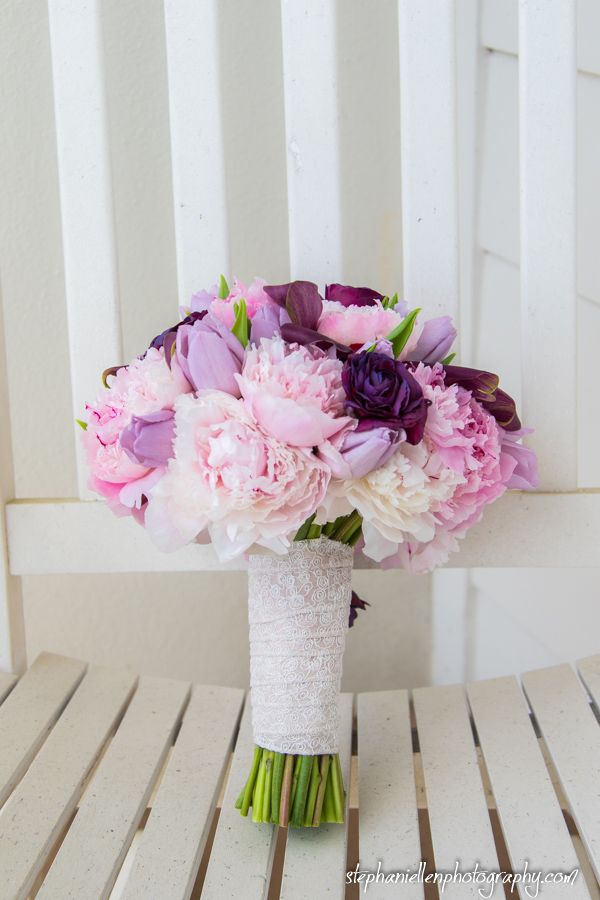 Beautiful bridal bouquet of pink peonies and purple tulips wrapped in white lace.