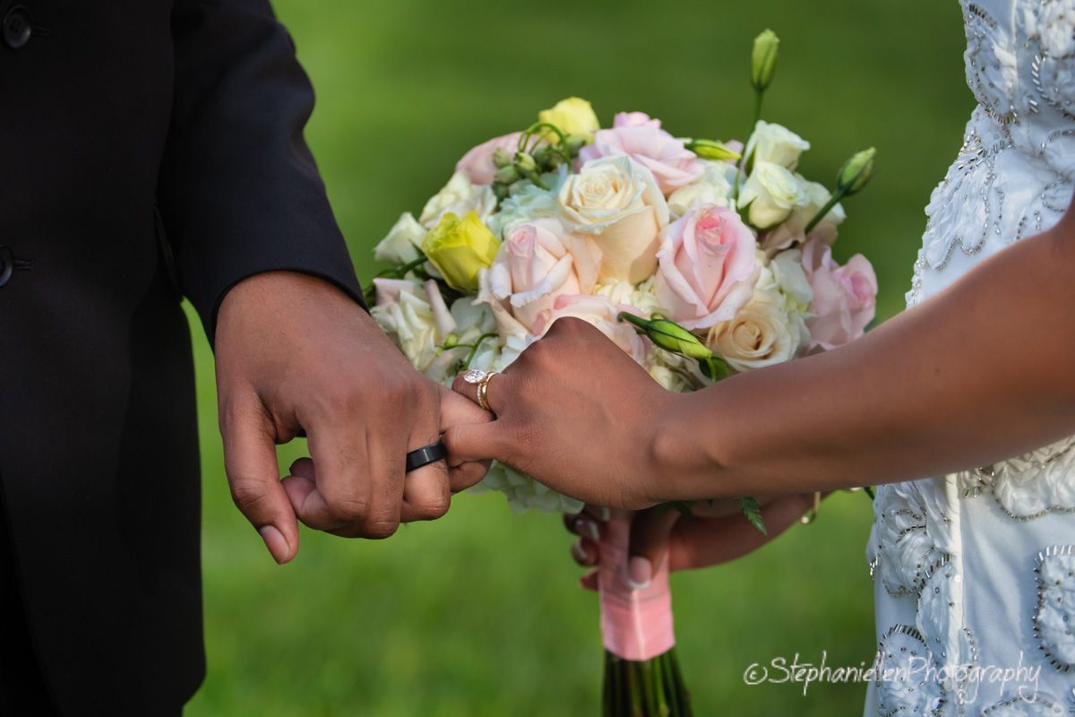 Close-up of couple exchanging rings with a pink and white rose bridal bouquet.