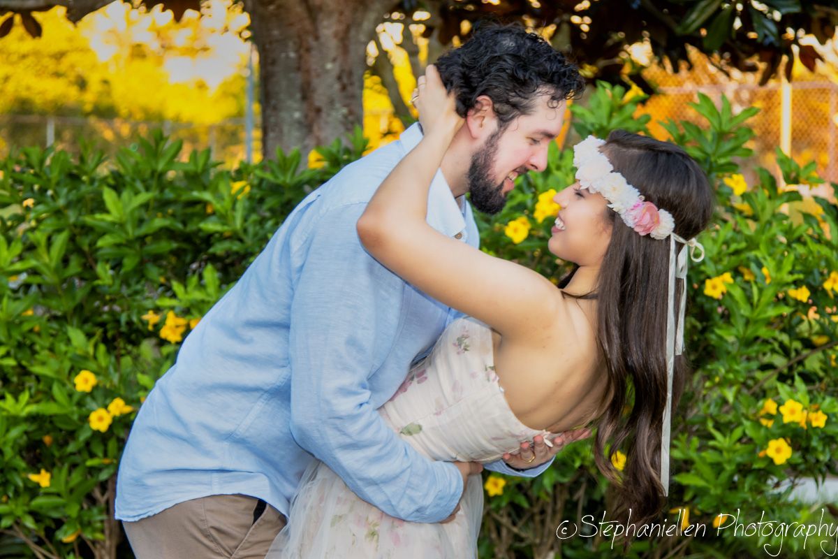 Couple shares a joyful dance embrace among vibrant yellow flowers in a lush garden at sunset.