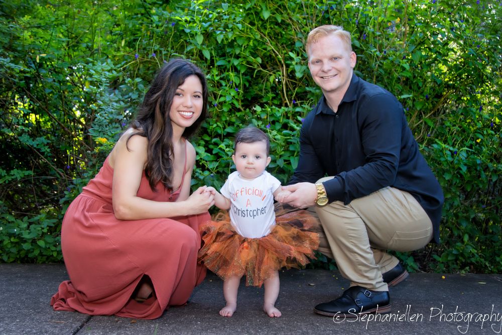 Family portrait of parents holding hands with their baby in a tutu outdoors, taken by StephanieEllen Photography.