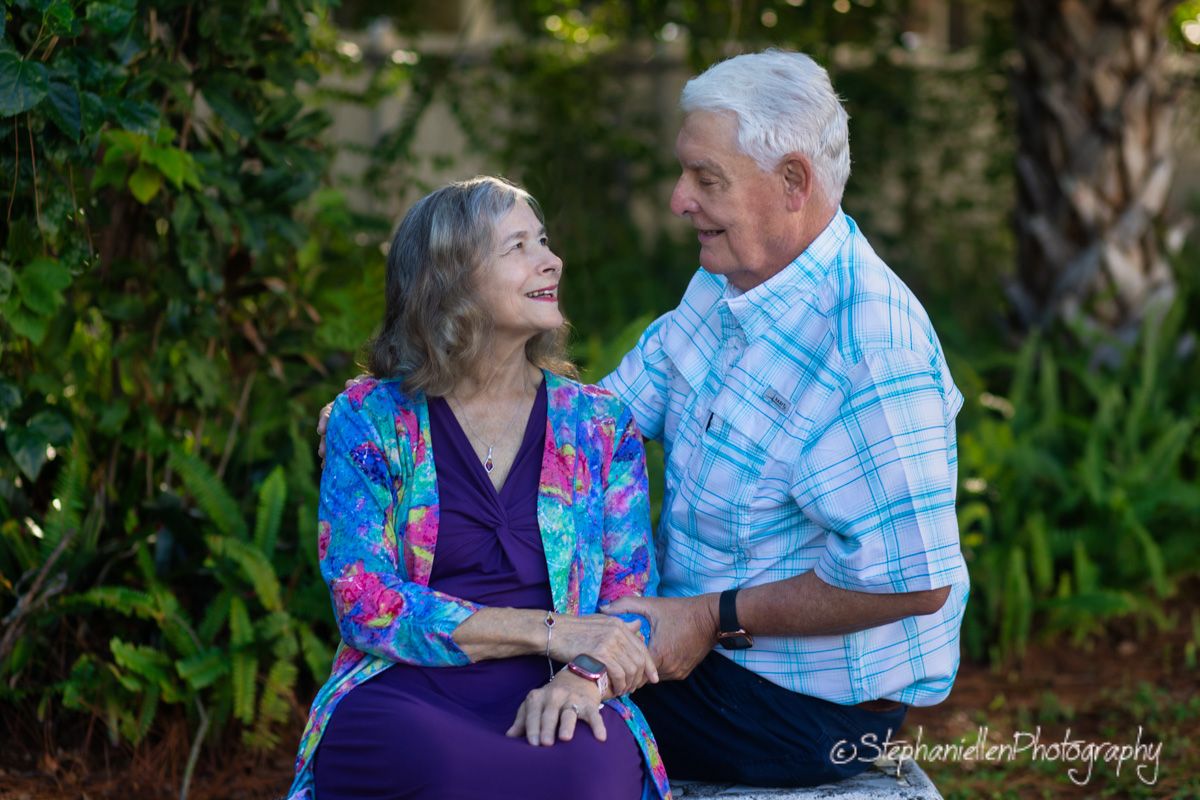 Elderly couple sharing a loving glance while seated together in a lush garden setting.