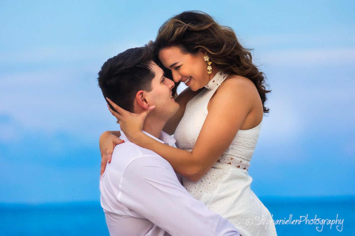 Happy couple embracing and laughing together against bright blue sky background.