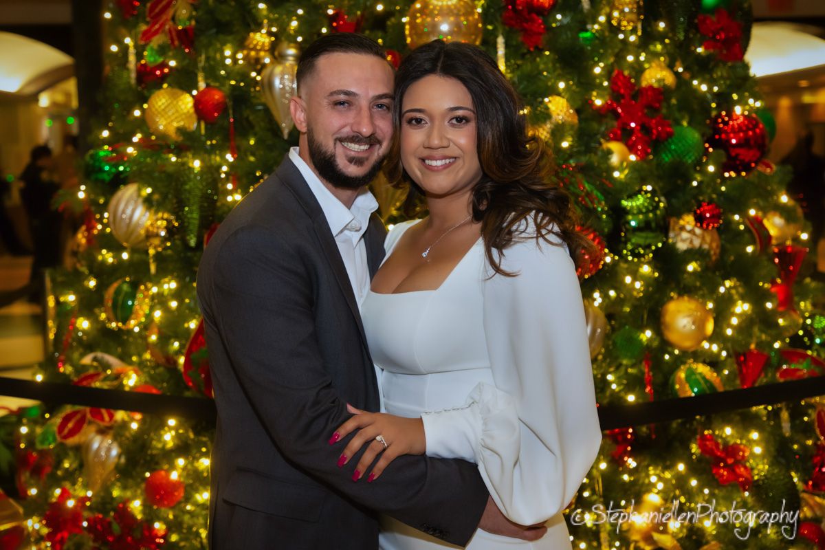 Smiling couple posing together in front of a decorated Christmas tree with colorful ornaments.