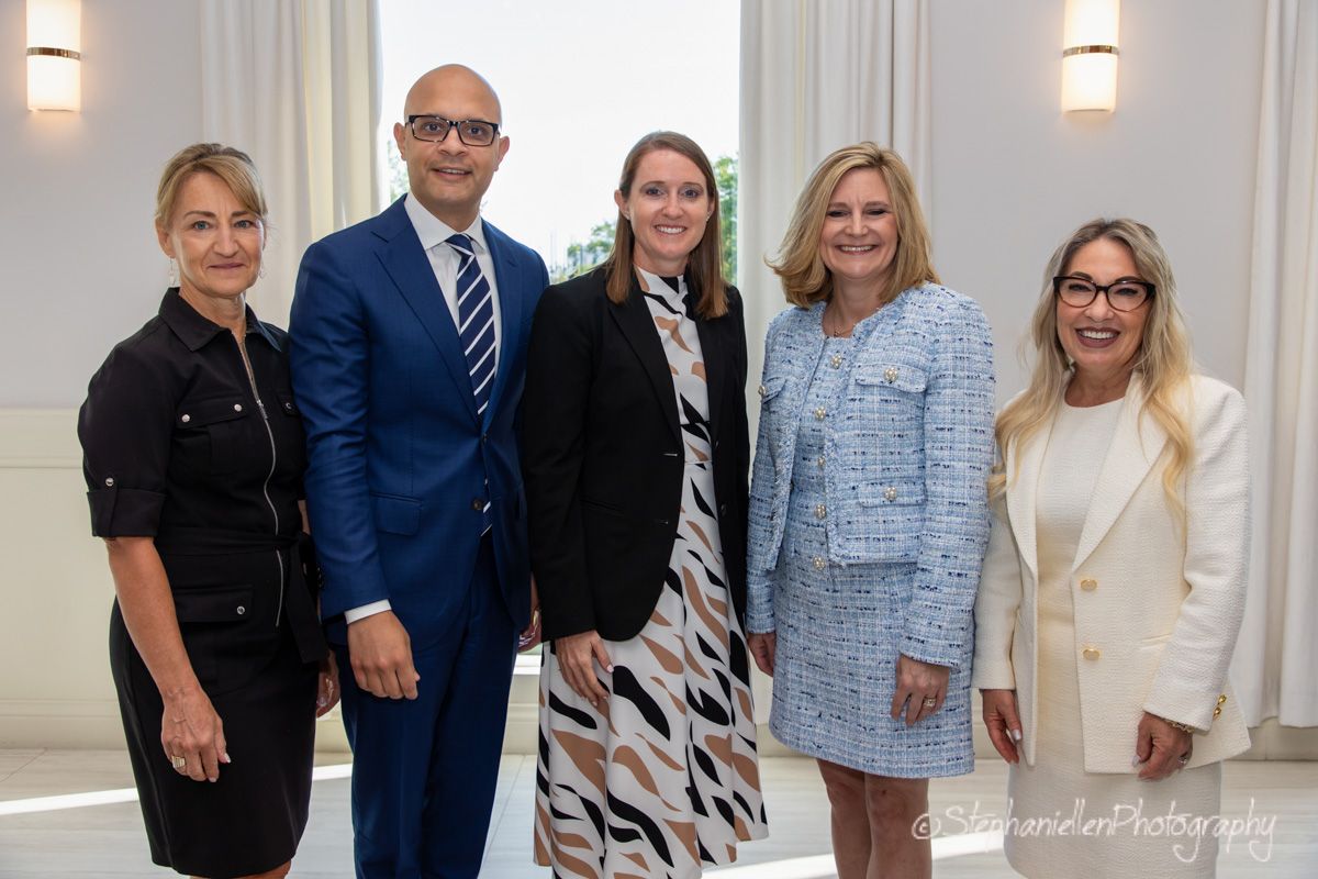Five professionally dressed business people posing together at a formal event.