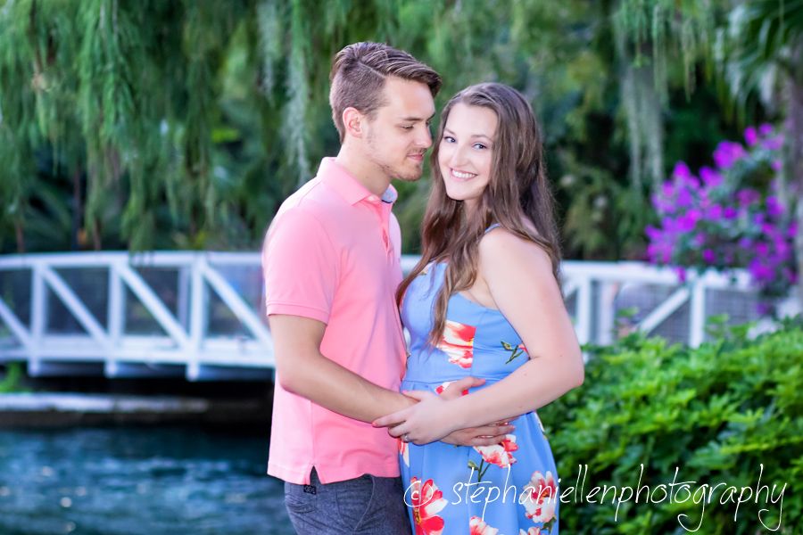Romantic couple embracing outdoors near a tranquil pond with lush green foliage backdrop.