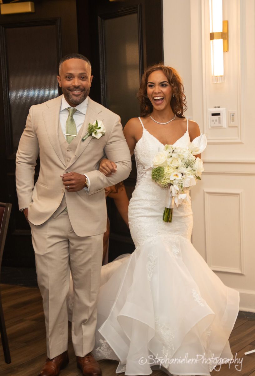 Smiling bride and groom walk arm in arm down the aisle in elegant wedding attire.