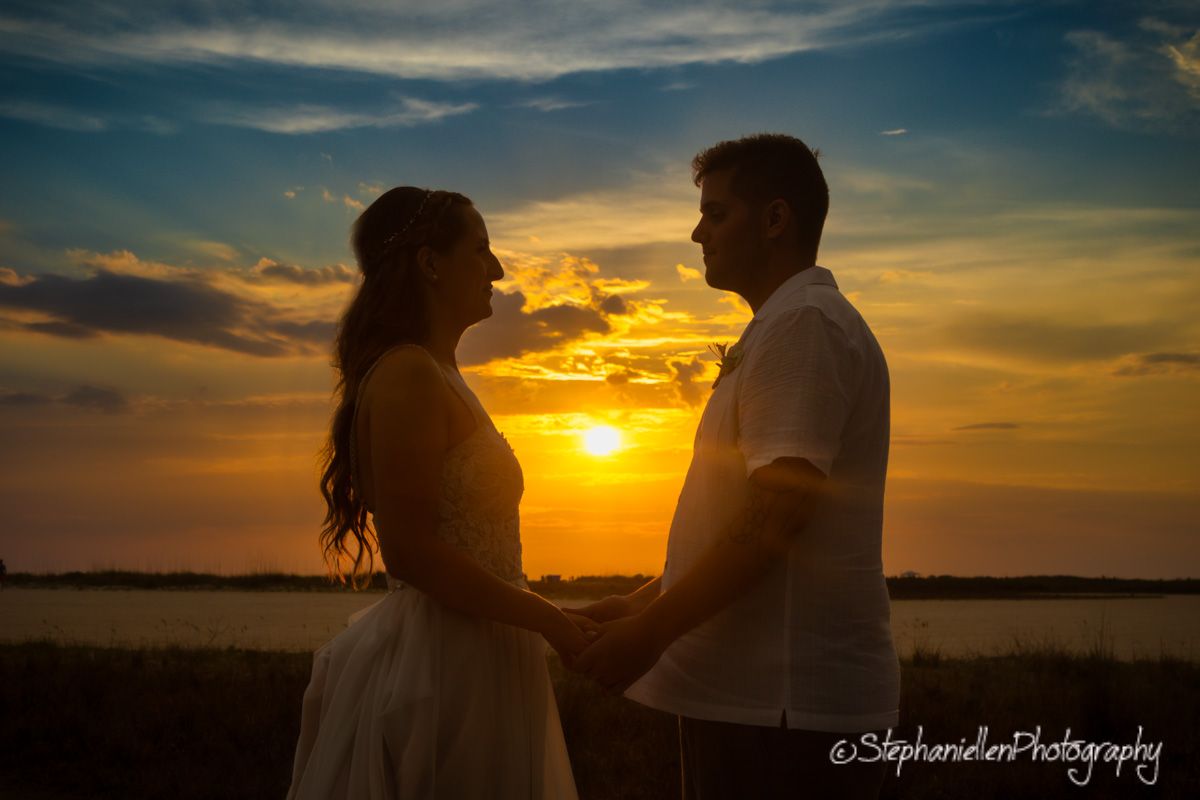 Couple holds hands facing each other in romantic silhouette against vibrant sunset sky.