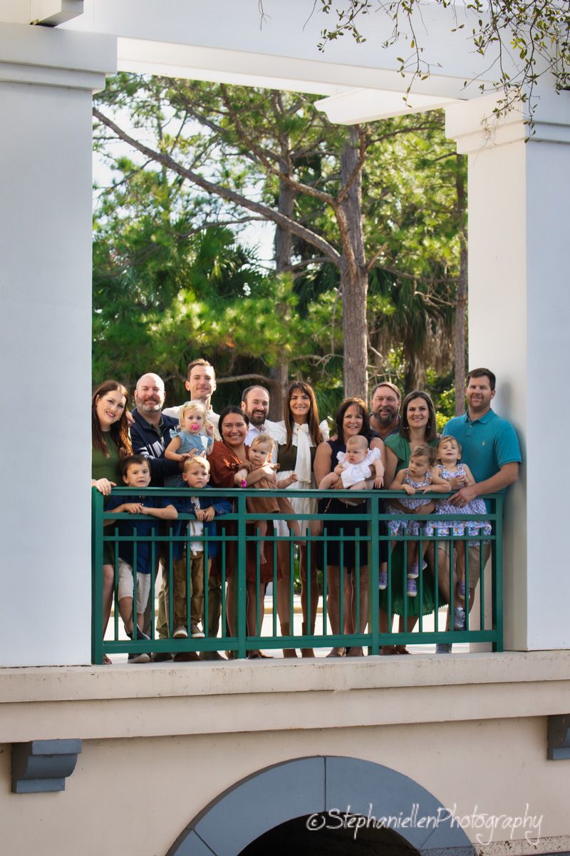 Large family group portrait on a balcony surrounded by lush green trees.