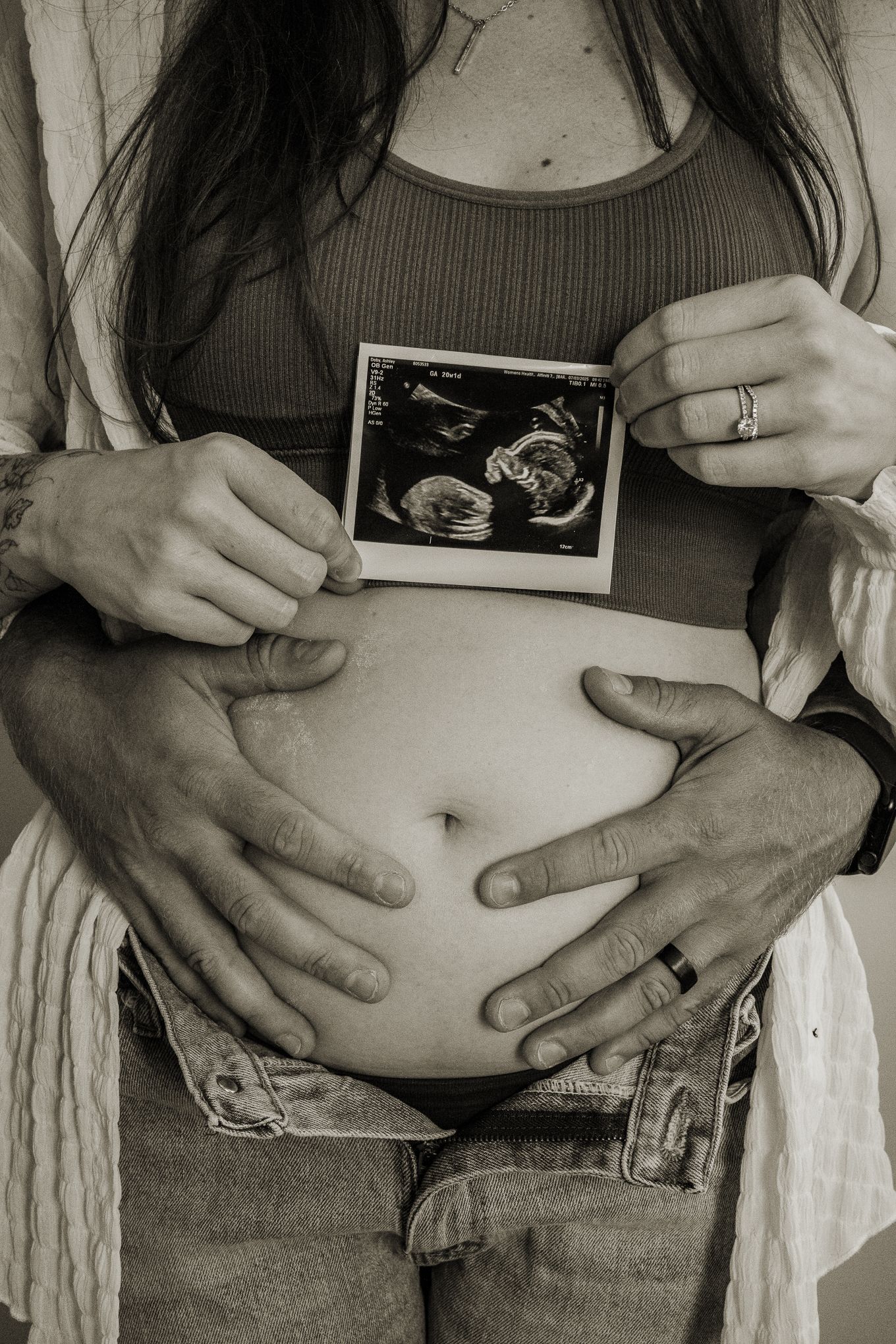 Couple holding ultrasound photo over pregnant belly in black and white photo.