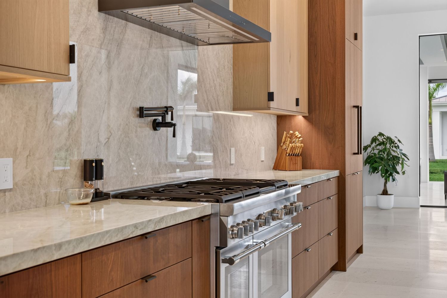 Luxury kitchen featuring professional gas range, marble backsplash, wood cabinetry, and quartz countertops.