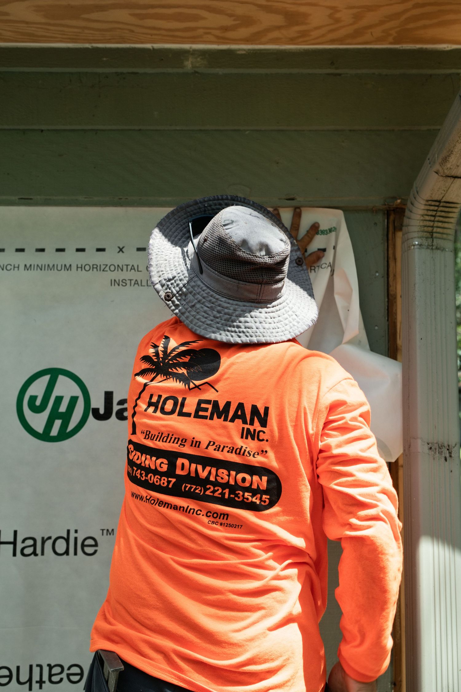 Holeman Inc construction worker in orange safety shirt installing James Hardie siding on building exterior.