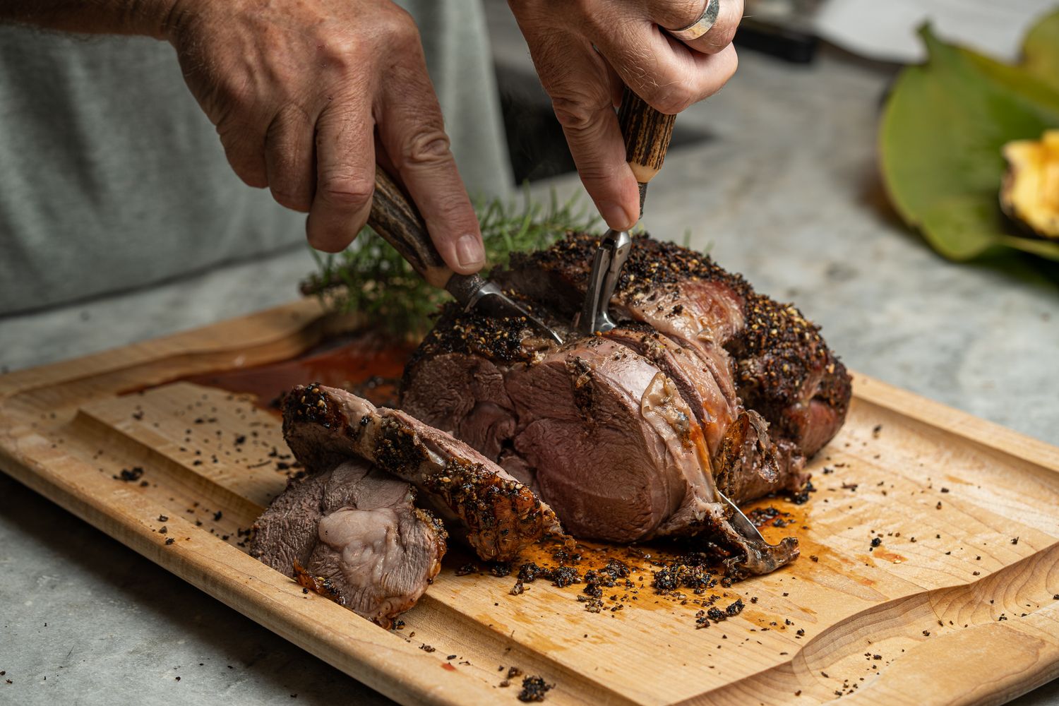 Chef carving a herb-crusted roasted leg of lamb on a wooden cutting board.