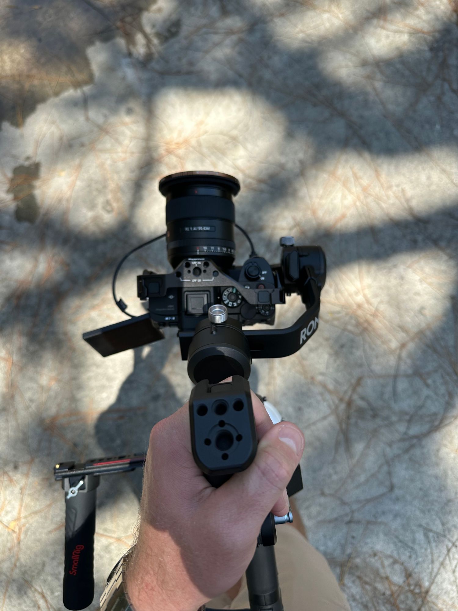 Hand holding camera gimbal stabilizer with mirrorless camera and wide angle lens outdoors.