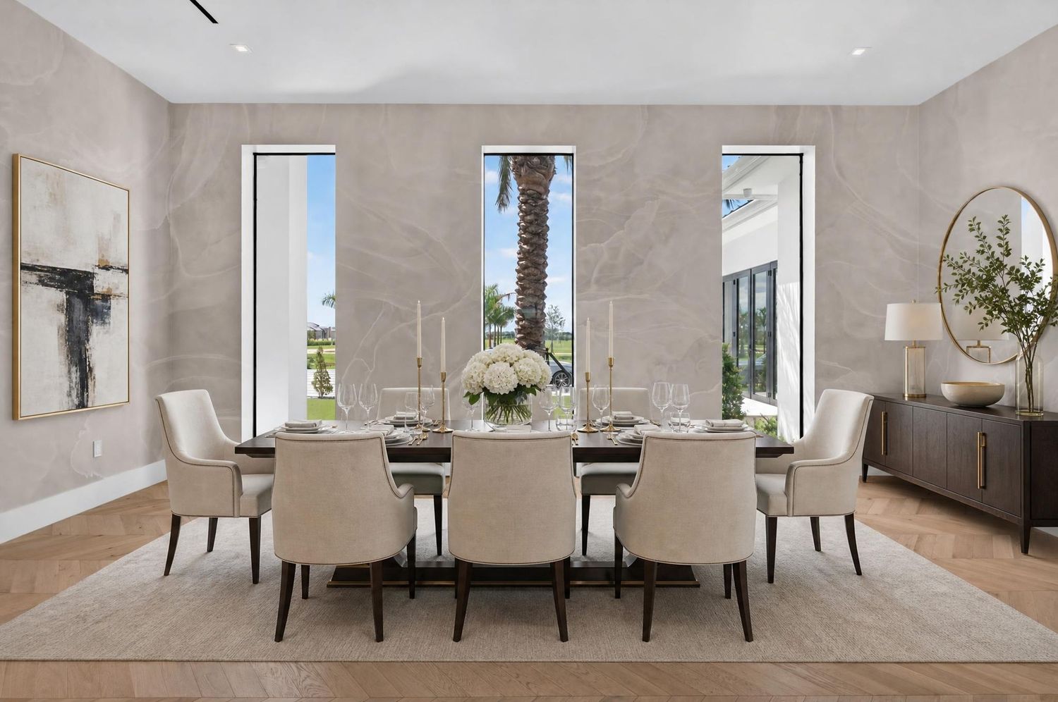 Elegant dining room with marble accent walls, tall windows, upholstered chairs, and floral centerpiece on table.