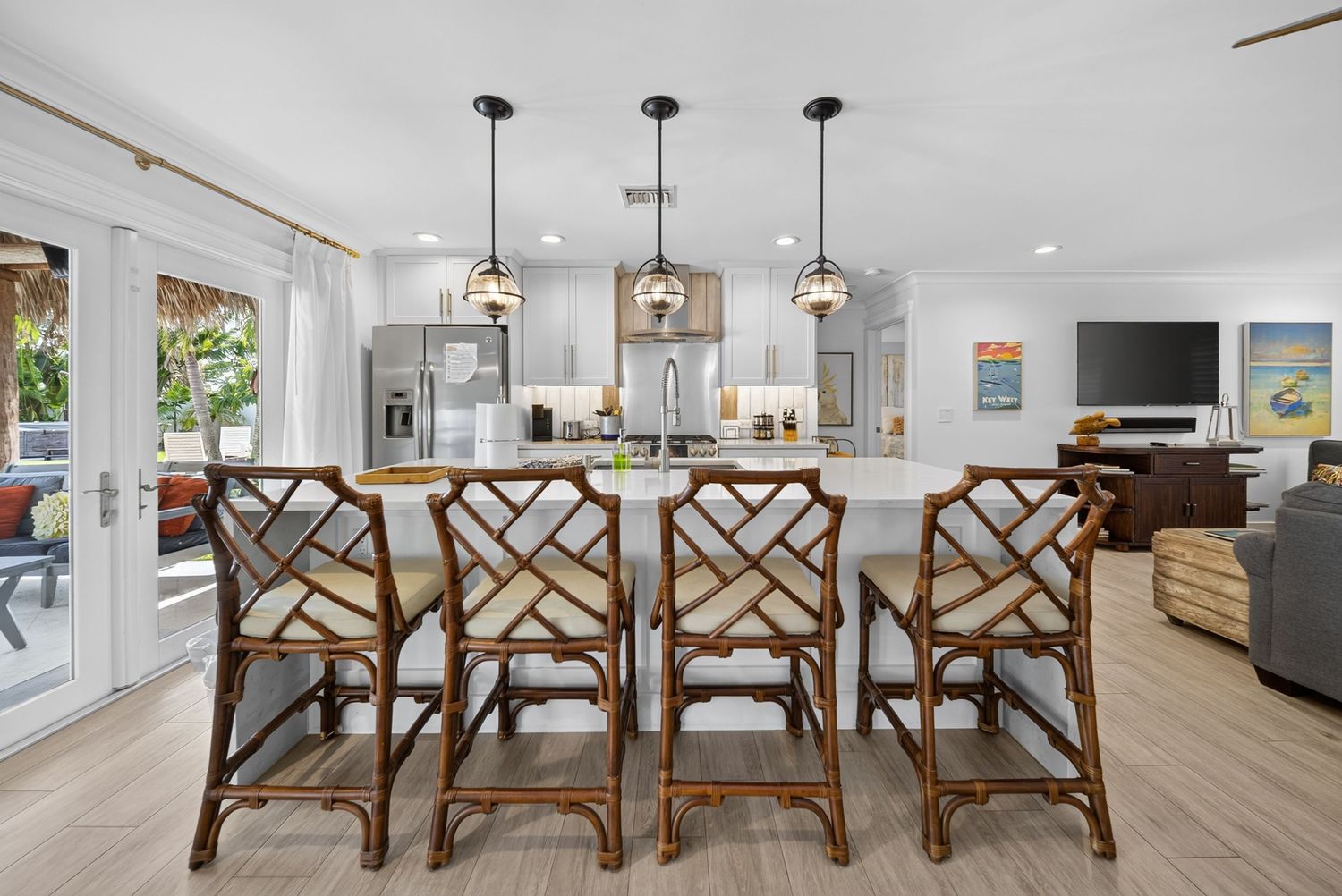 Bright open kitchen with rattan bar stools, white cabinets, pendant lights, and living area.
