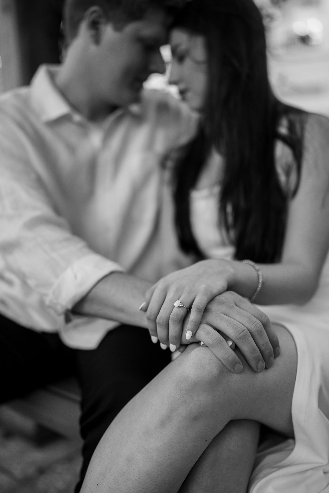 Black and white close-up of engaged couples hands showing diamond ring while sitting together.