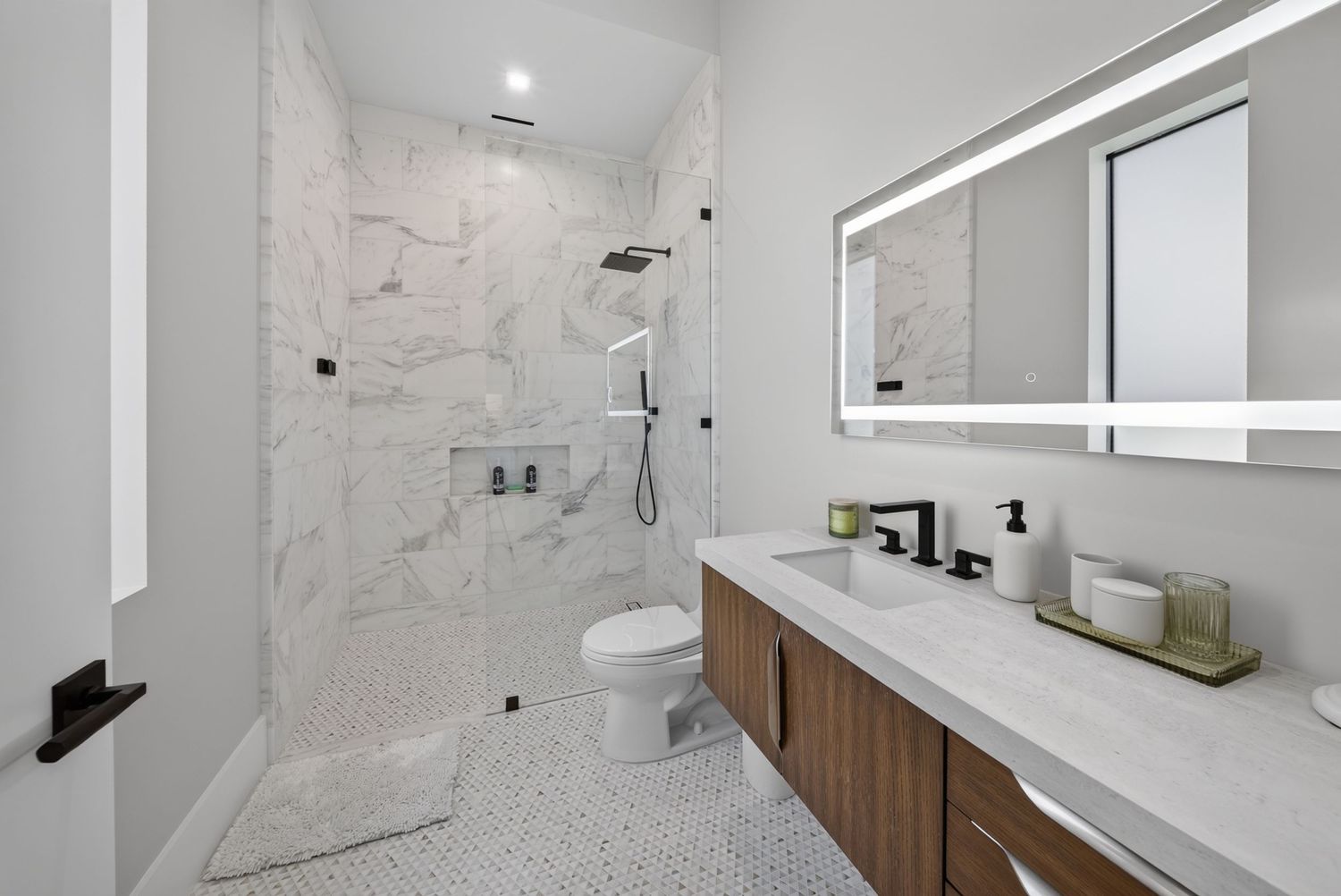 Luxury marble bathroom with walk-in shower, backlit mirror, and walnut vanity with black fixtures.