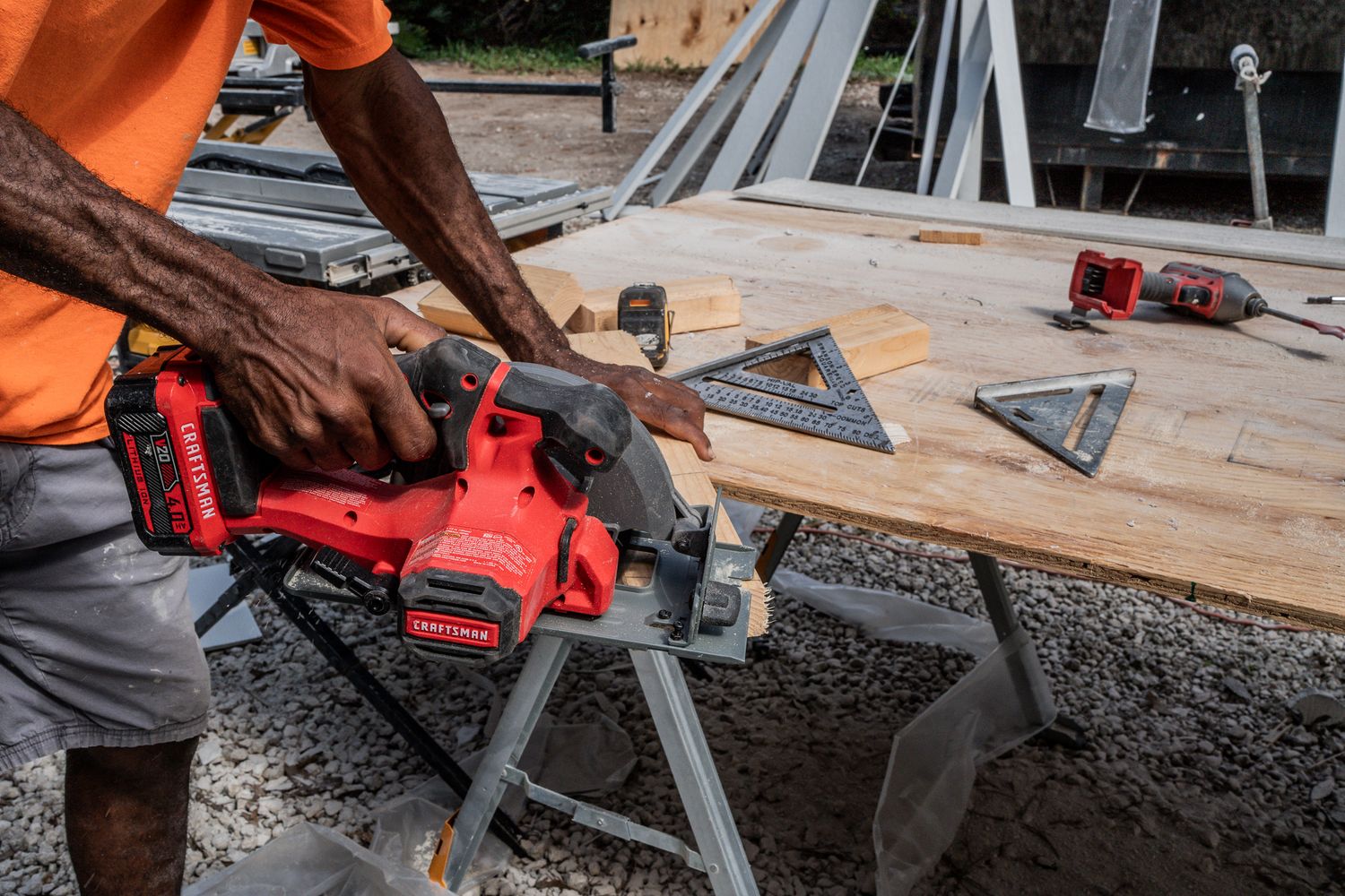 Close-up of worker using red Milwaukee circular saw to cut wood with speed square guide.