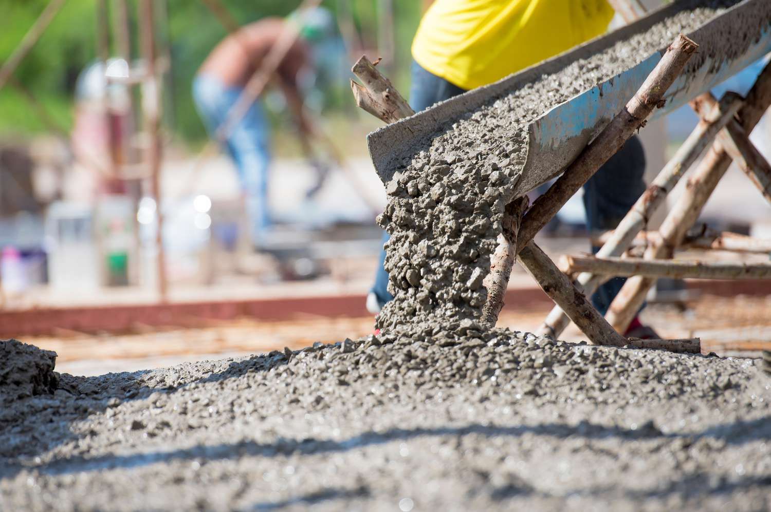 Construction worker pouring wet concrete from wheelbarrow at building foundation site.