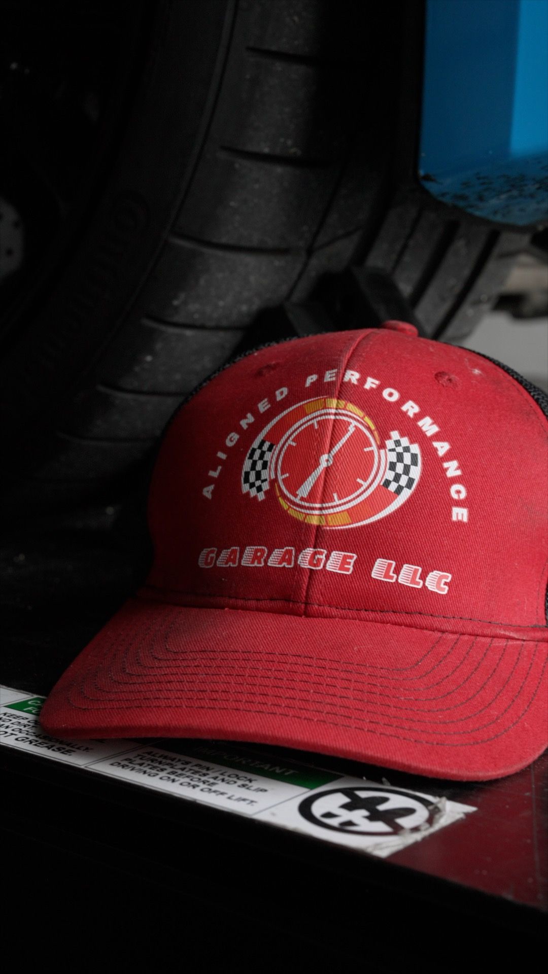 Red Aligned Performance Garage LLC embroidered logo baseball cap displayed near tires.