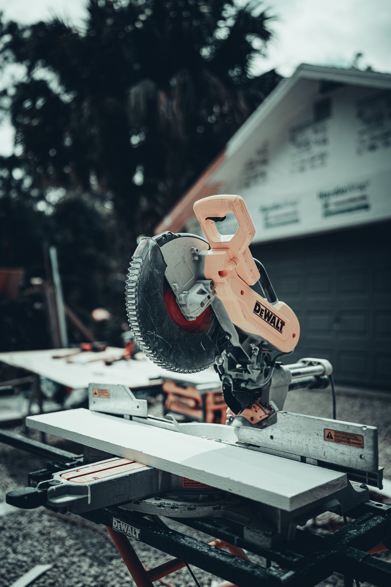 DeWalt miter saw on a stand outdoors with a building and trees in the blurred background.