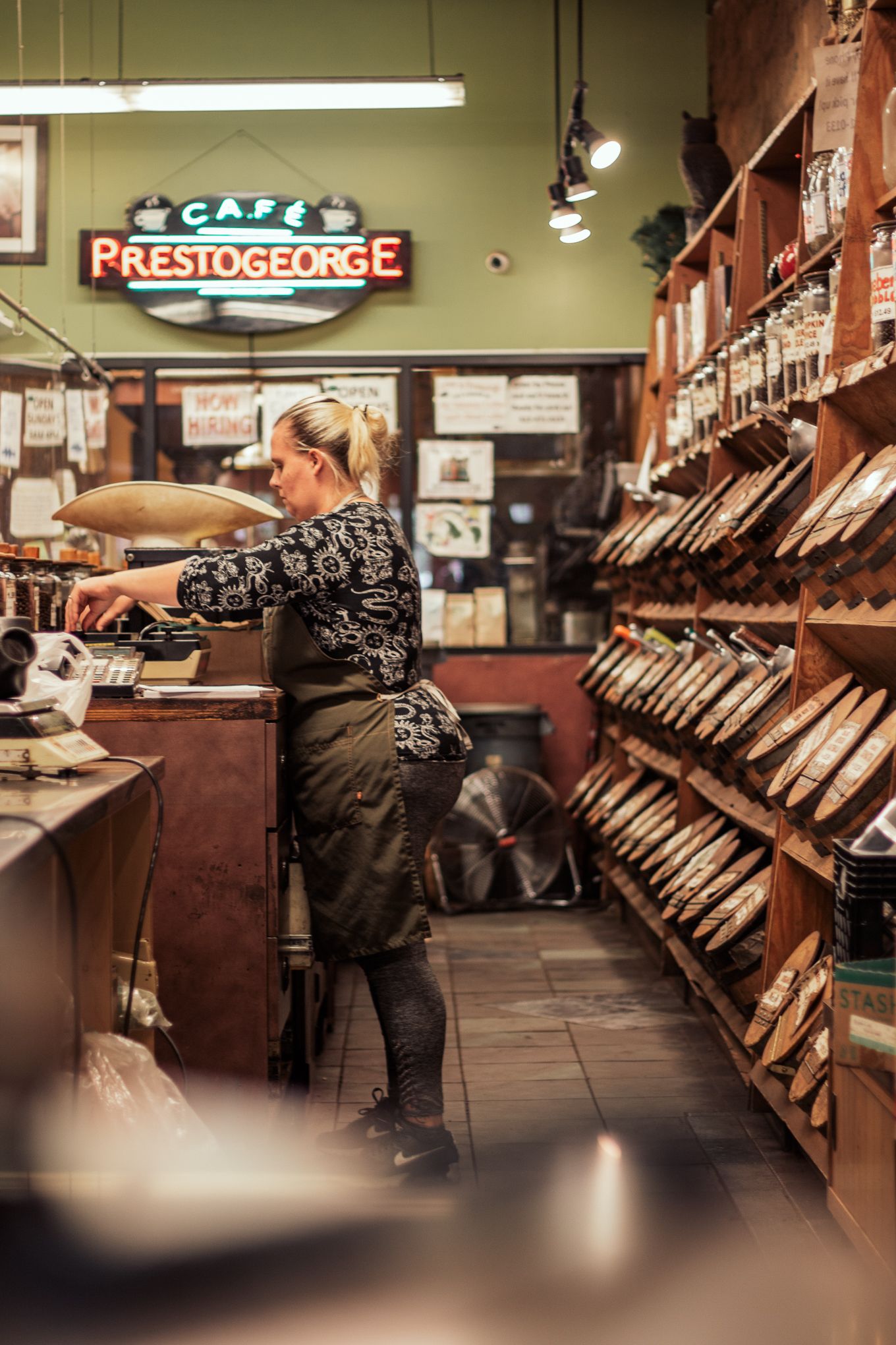 Female barista working behind counter at Cafe Prestogeorge coffee and tea shop interior.