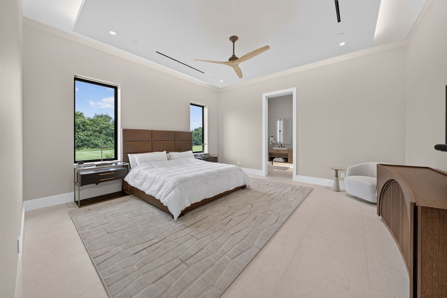 Elegant master bedroom with tray ceiling, ceiling fan, wood headboard, and large windows with garden views.