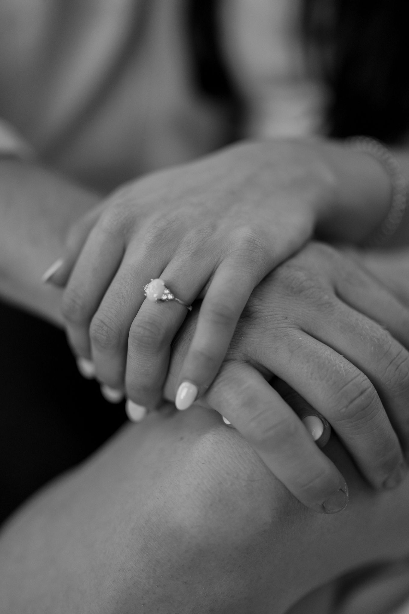 Black and white close-up of hands with elegant engagement ring on woman's finger.