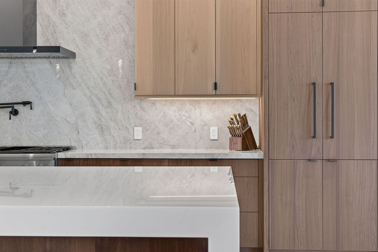 Modern kitchen featuring light wood cabinetry, marble backsplash, and quartz countertops.