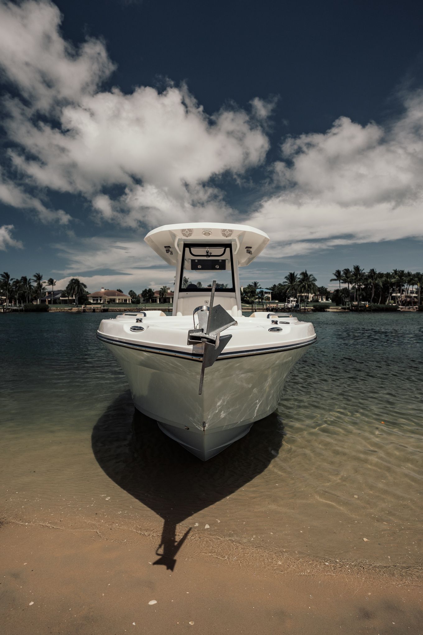 White center console fishing boat beached on sandy shore with tropical palm trees and cloudy sky.
