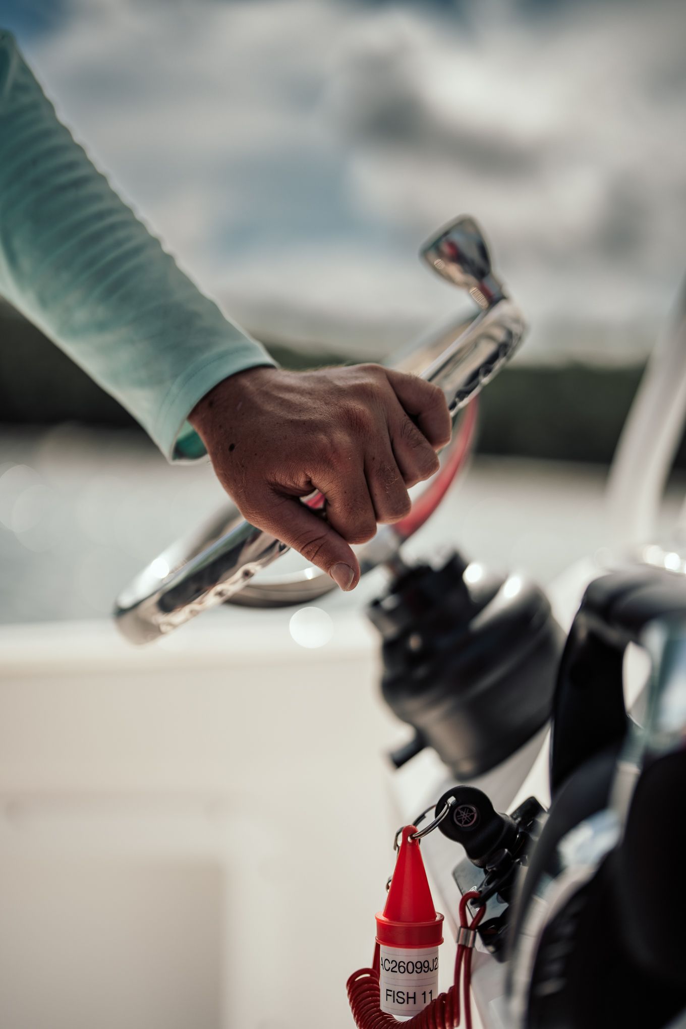 Close-up of a hand gripping a boat throttle control with a red safety lanyard attached.
