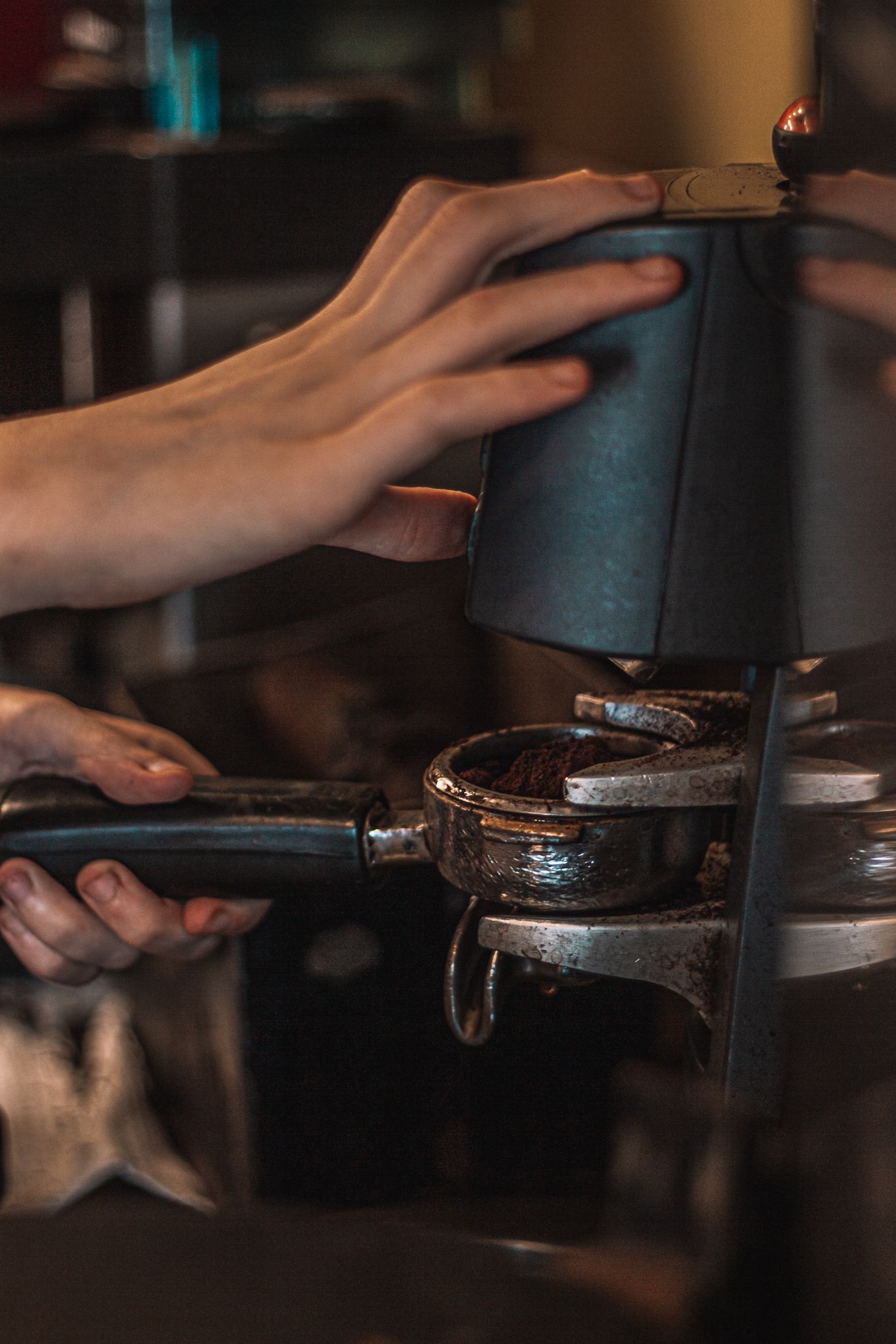 Barista using a coffee tamper to press espresso grounds into a portafilter at a cafe.