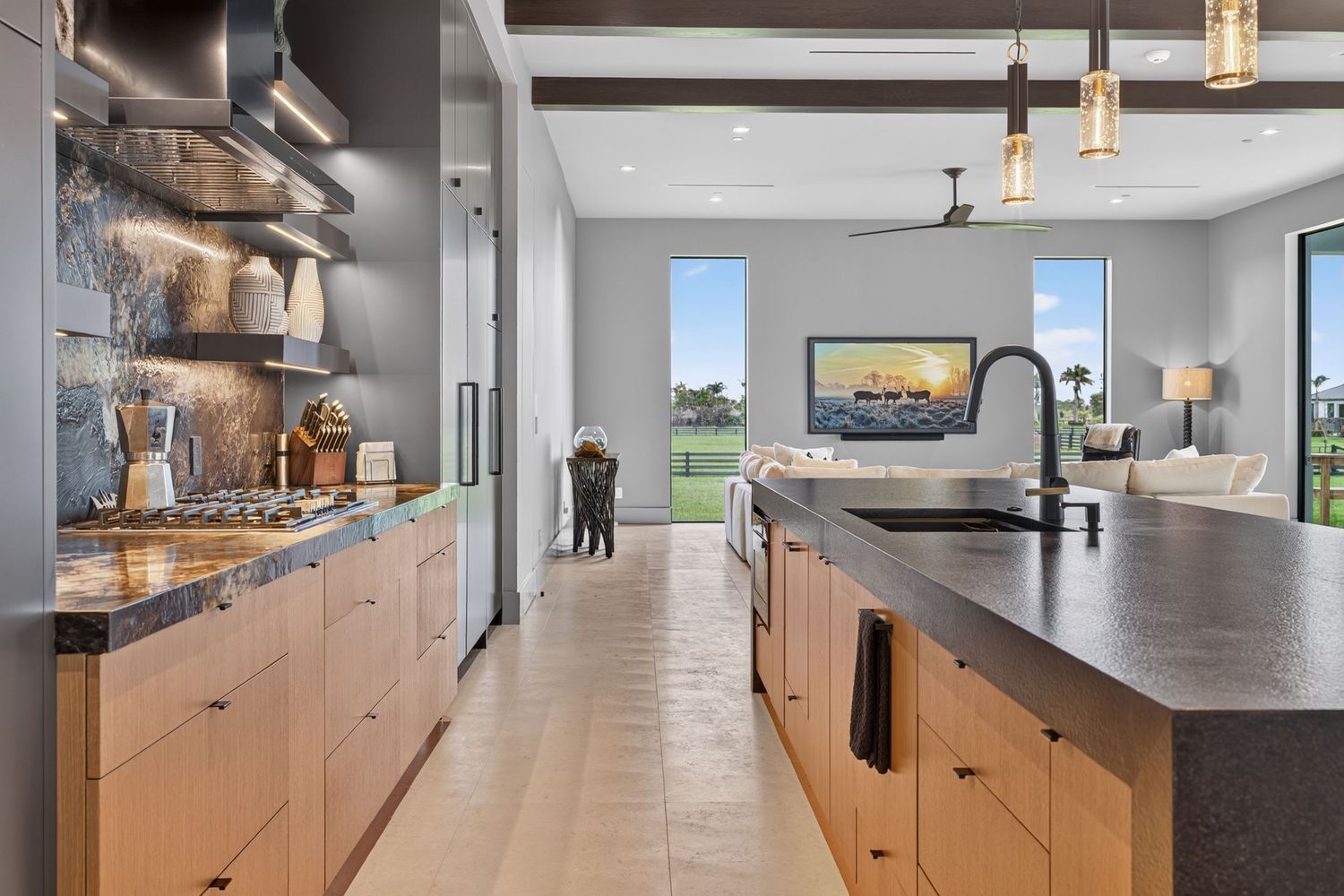Modern open-concept kitchen with wood cabinetry, black countertops, and views to living area.