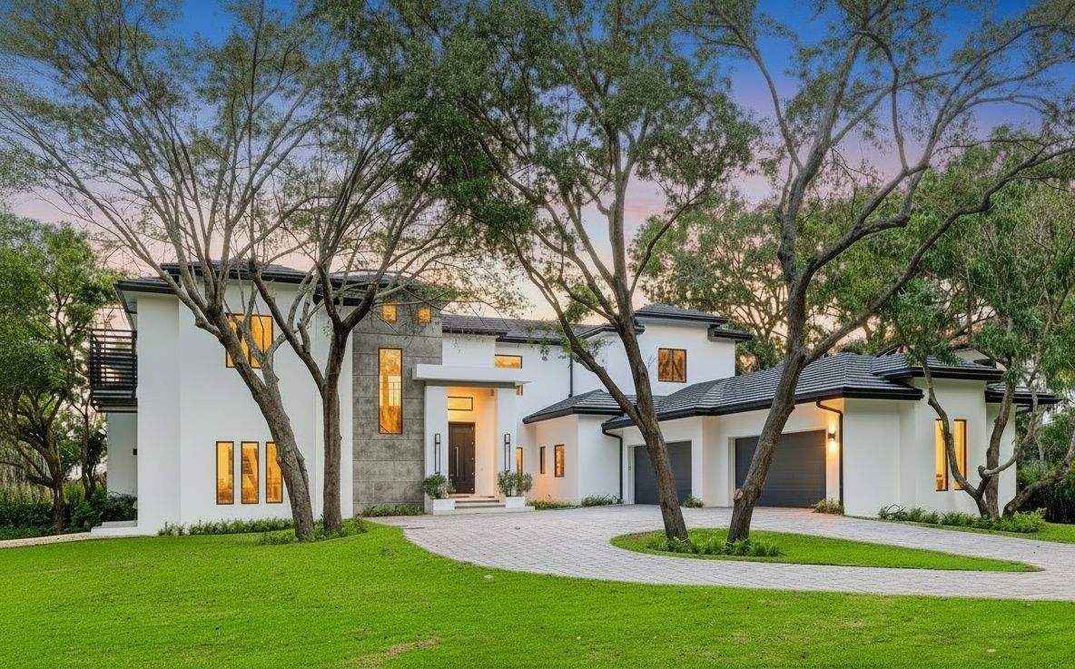 Beautiful white contemporary home with dark roof nestled among tall mature trees at golden dusk hour.