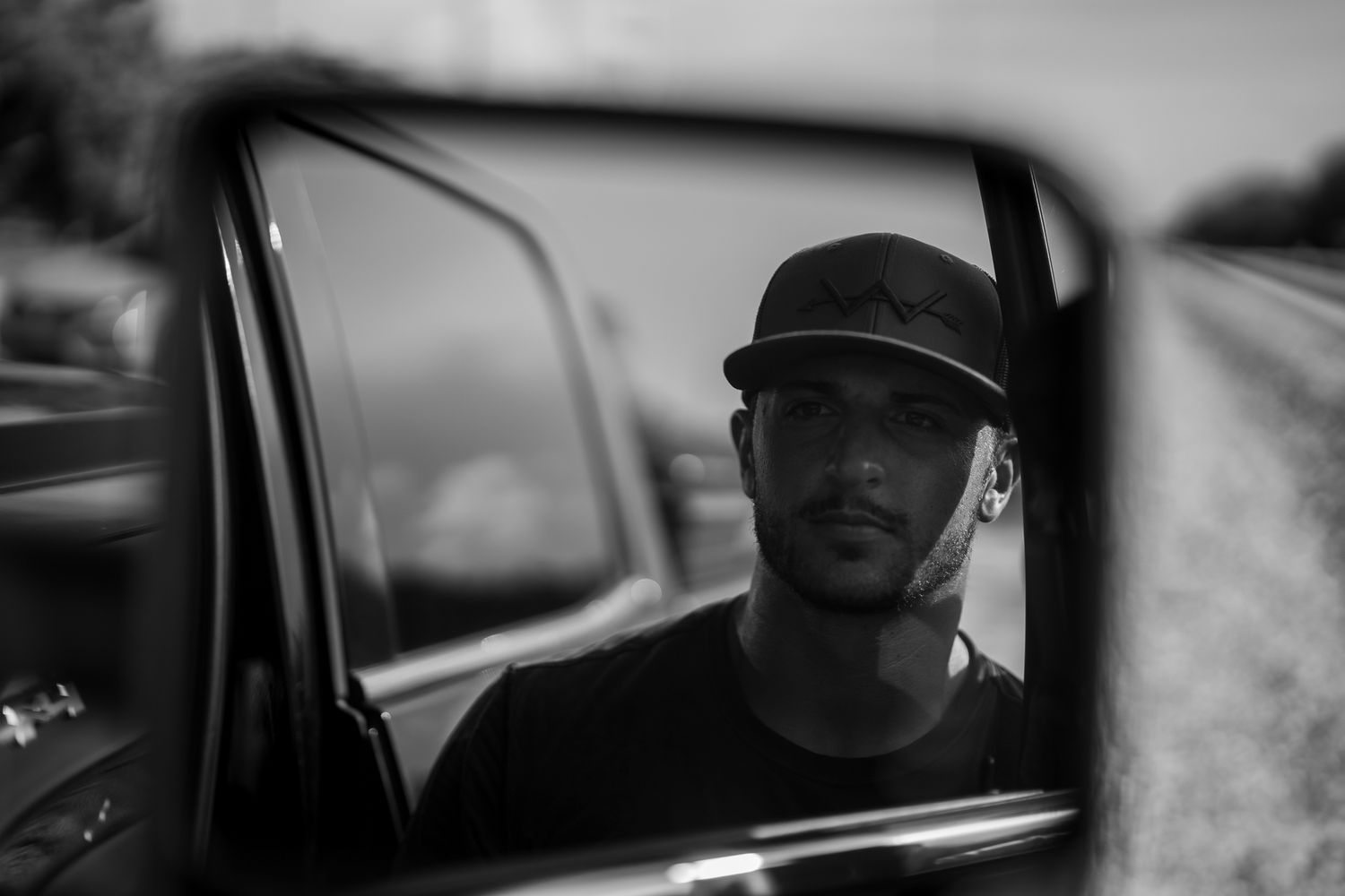 Black and white portrait of young man with cap reflected in vintage truck side mirror outdoors.