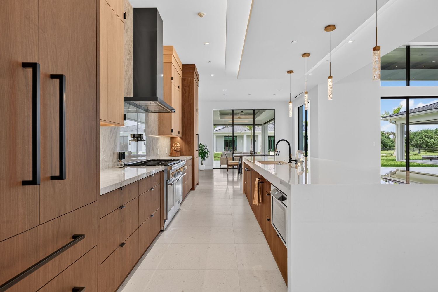 Modern kitchen with wood cabinetry, island, pendant lights, range hood, and floor-to-ceiling windows.
