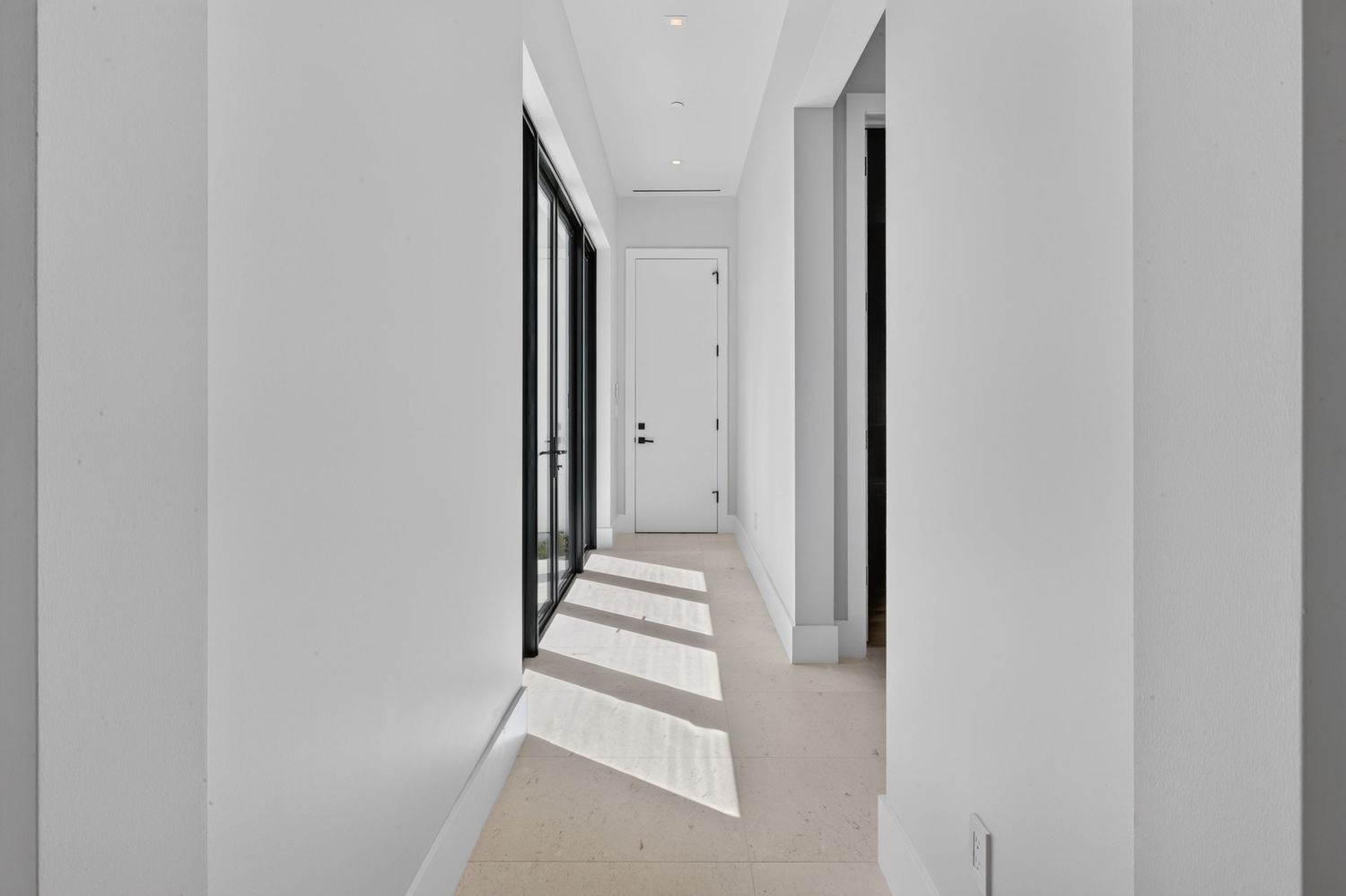 Modern bright white hallway with black-framed windows casting shadows on light wood floors.