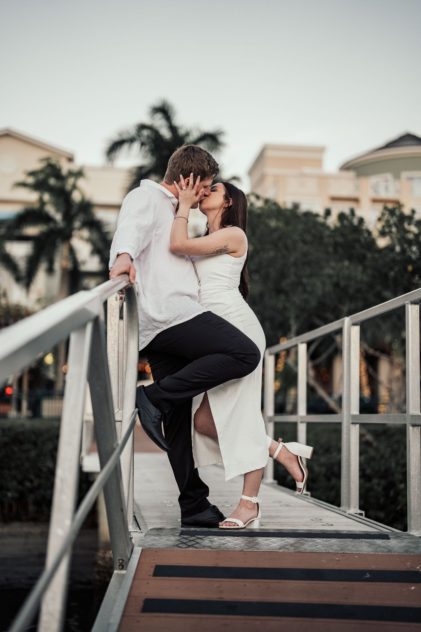 Romantic couple sharing passionate kiss on wooden bridge at tropical resort at dusk.