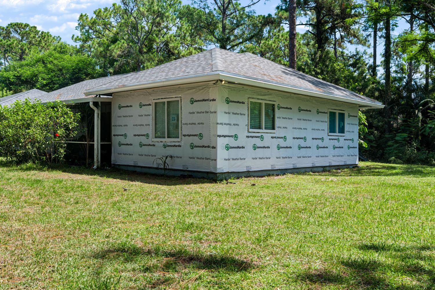 Small residential home exterior wrapped in James Hardie weather barrier house wrap, surrounded by trees.