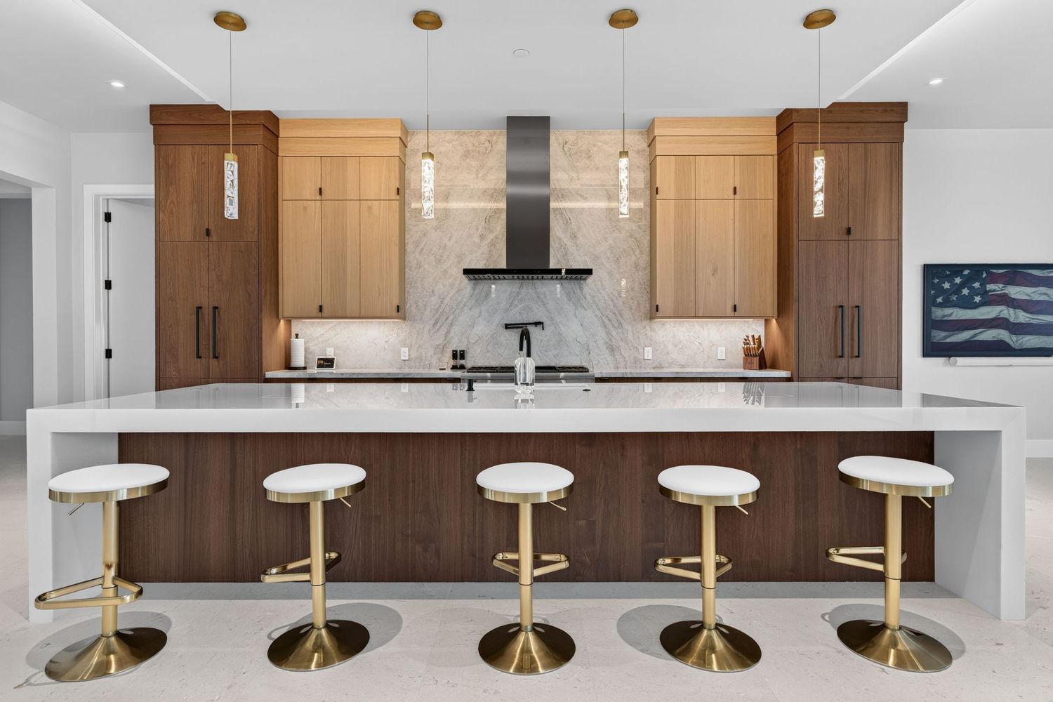 Modern kitchen with walnut cabinets, marble backsplash, white island, and gold bar stools.