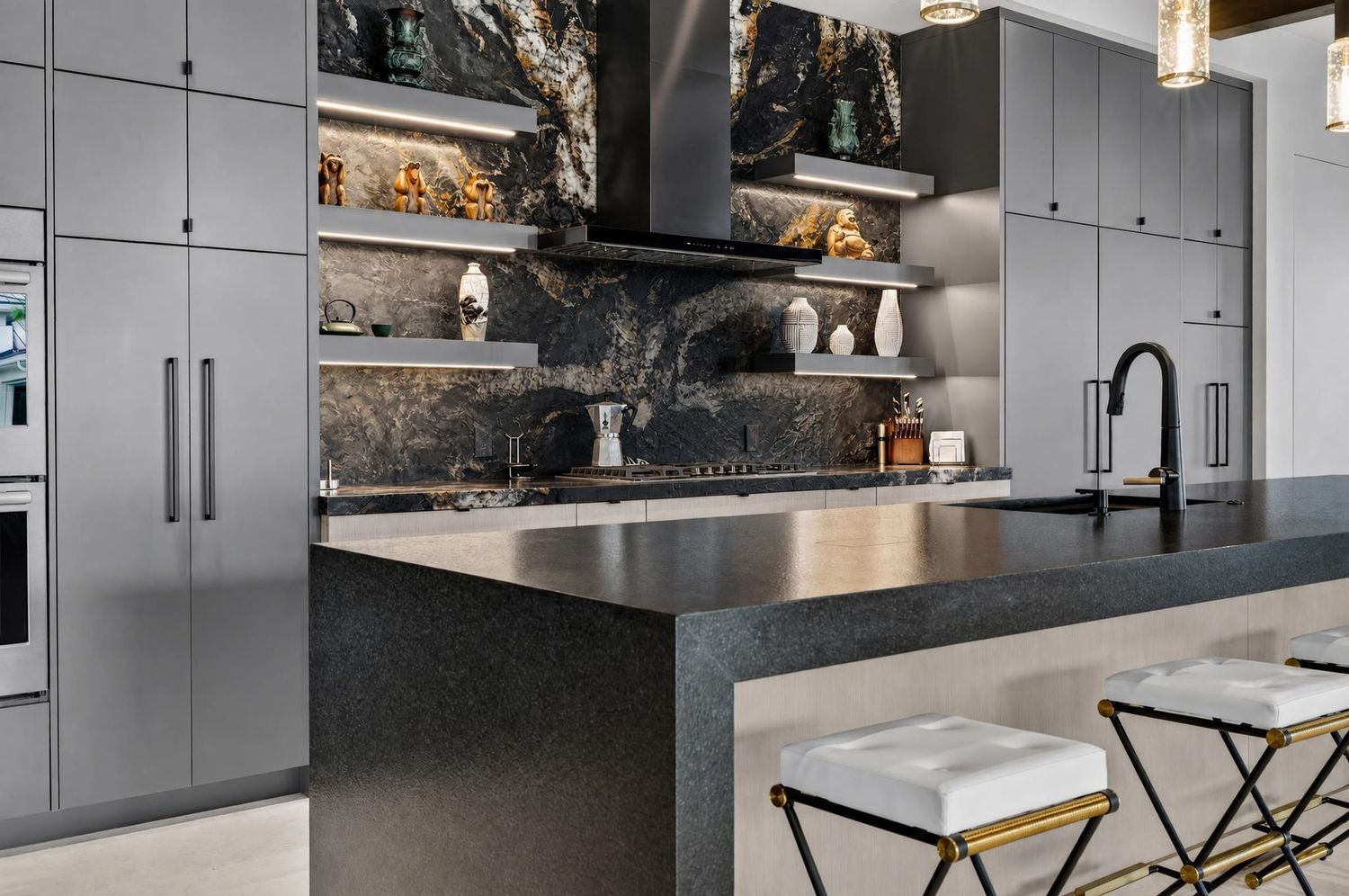 Sleek gray kitchen with marble backsplash, stainless island, black faucet, and gold bar stools.