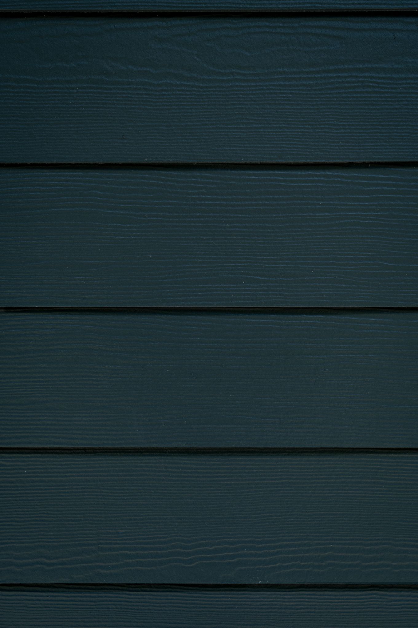 Close-up of dark teal James Hardie fiber cement lap siding with realistic wood grain texture.