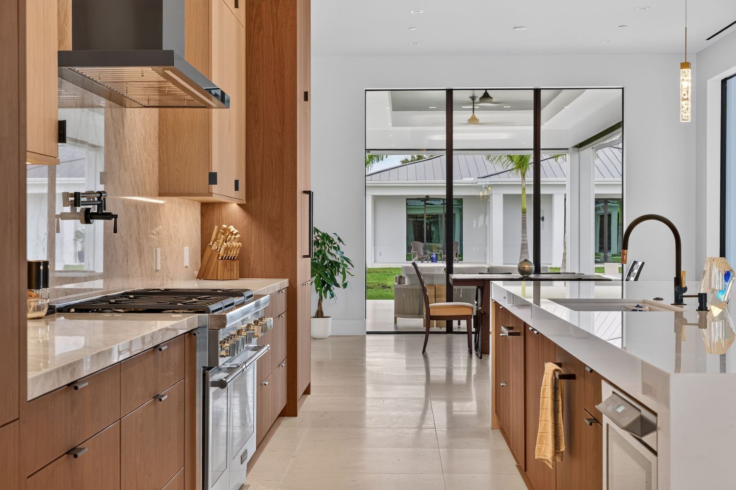 Gourmet kitchen with wood cabinetry, gas range, range hood, marble countertops, and view to outdoor patio.