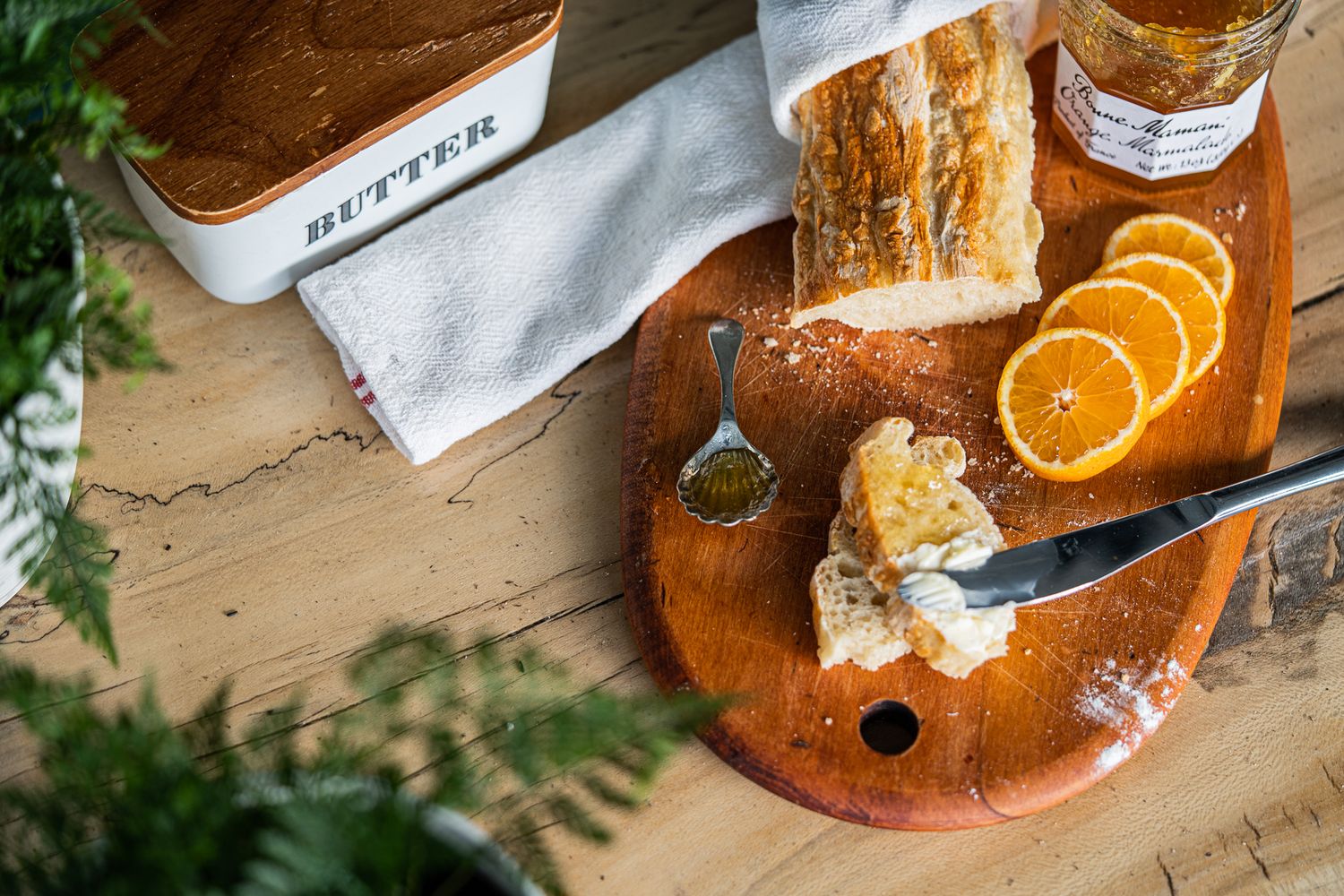 Rustic wooden board with sliced bread, orange slices, honey, and butter dish on table.