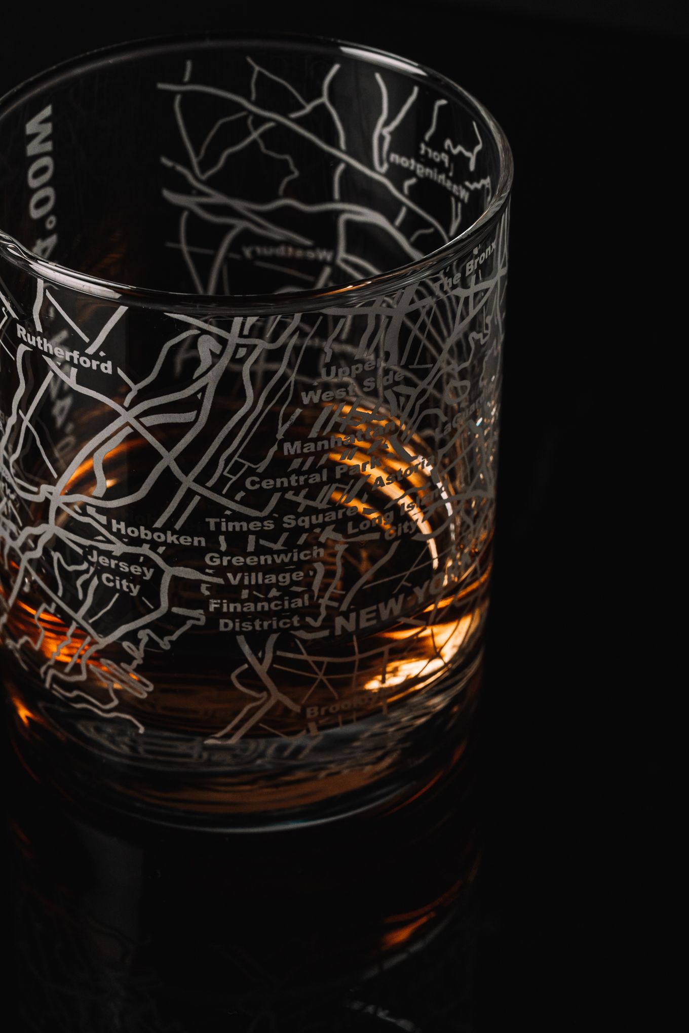 Close-up of engraved whiskey glass showing NYC landmarks map with Financial District and Hoboken details.